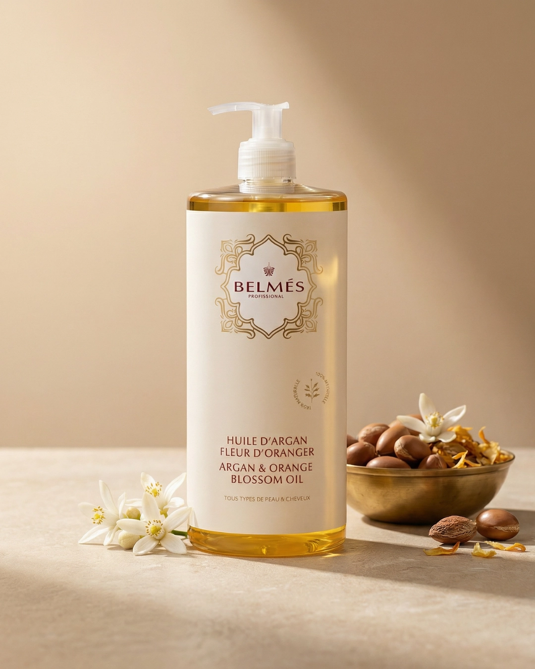 Flacon huile d'argan fleur d'oranger Belmés Profissional – noix d'argan fleurs blanches d'oranger et pétales dorés dans bol doré marocain en arrière-plan