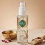 Flacon sérum L'Élixir de Lumière Belmés Profissional – bol doré marocain pétales de rose et poudre naturelle sur cuillère en bois en arrière-plan