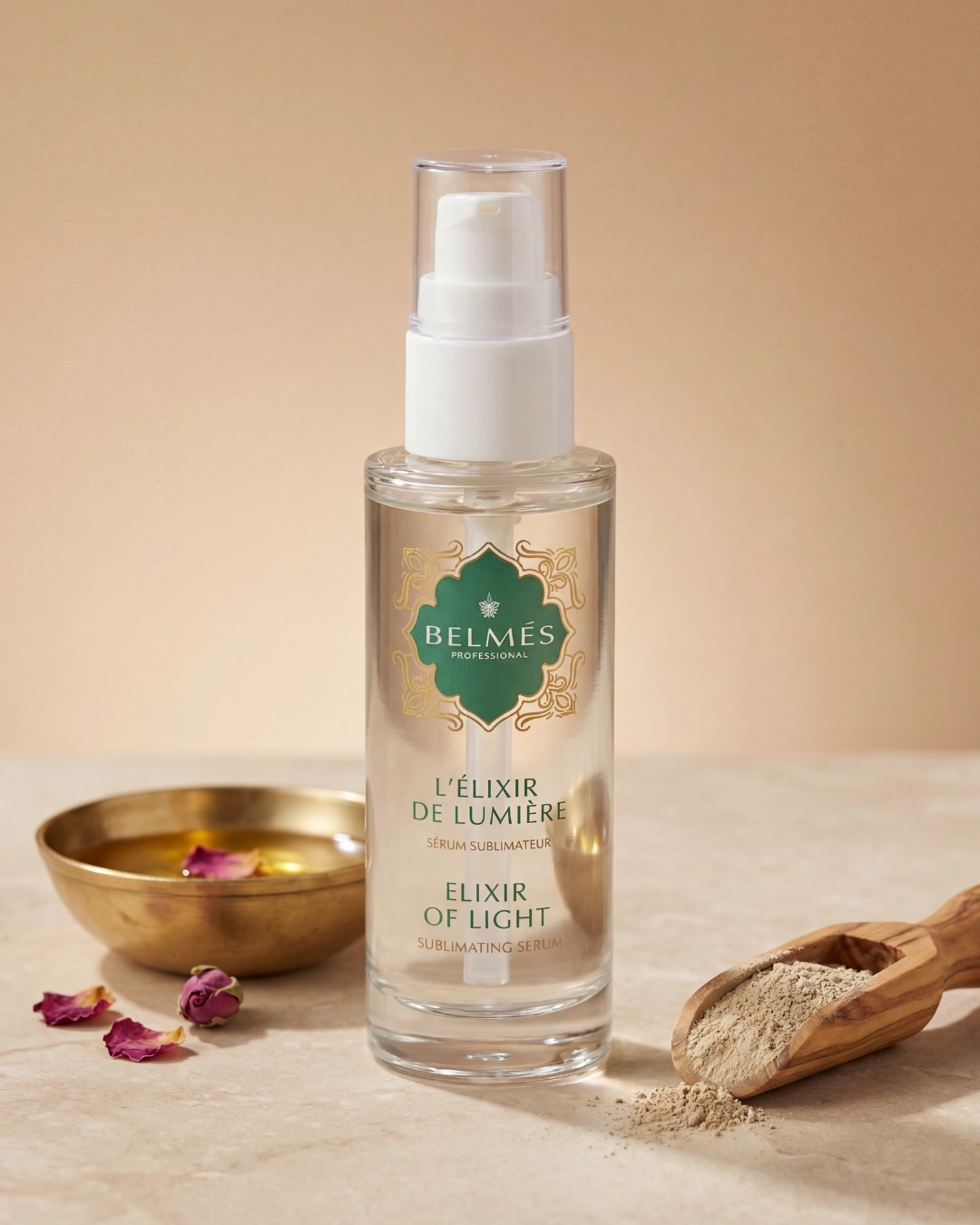 Flacon sérum L'Élixir de Lumière Belmés Profissional – bol doré marocain pétales de rose et poudre naturelle sur cuillère en bois en arrière-plan
