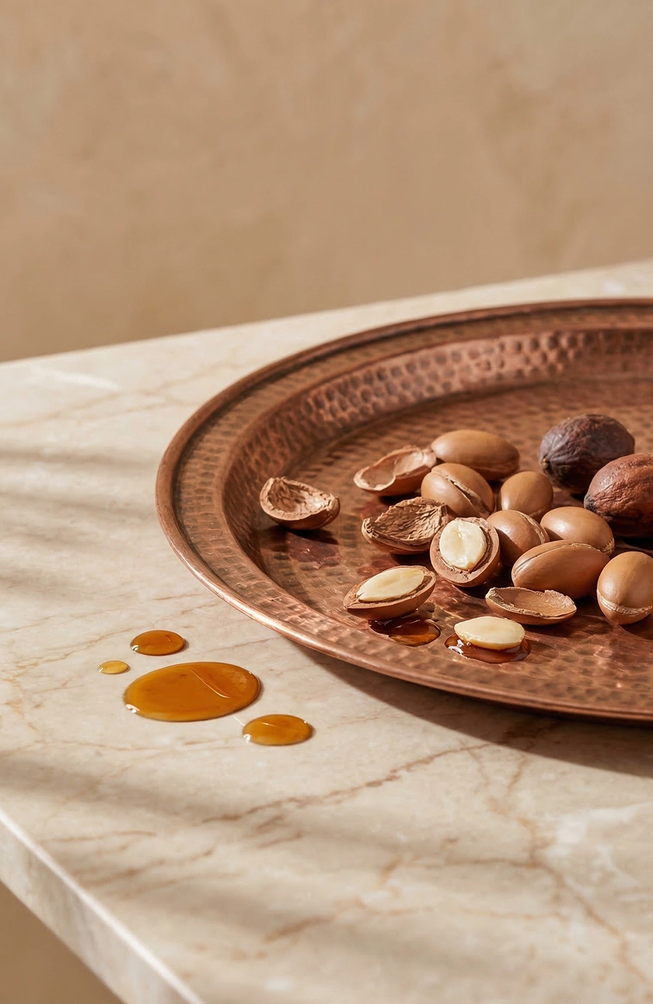 Noix d'argan entières et ouvertes sur plateau cuivré marocain martelé – gouttes d'huile dorée sur marbre ingrédient Belmés Profissional
