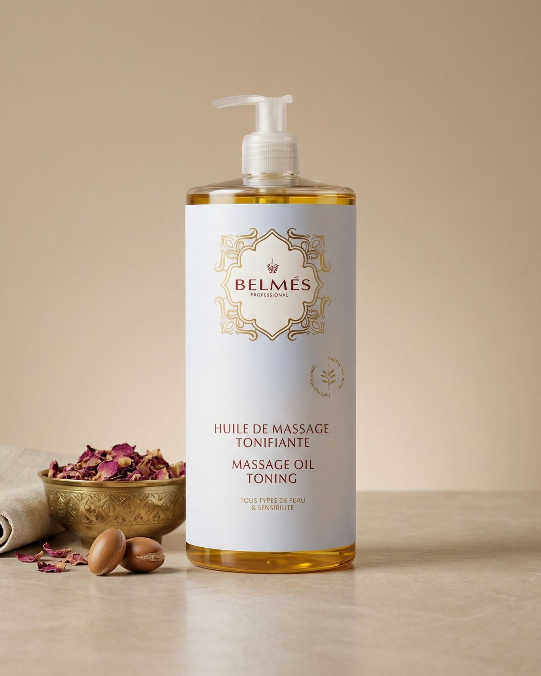 Flacon huile de massage tonifiante Belmés Profissional – bol doré marocain avec pétales de rose séchés et noix d'argan en arrière-plan